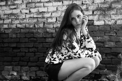 Portrait of confident woman couching against brick wall