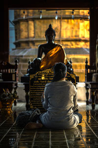 Rear view of woman sitting on floor against statue in temple