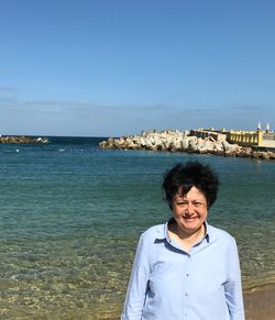 Portrait of smiling woman standing by sea against blue sky