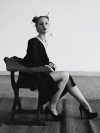 Portrait of sensuous woman wearing dress while sitting on chair against wall