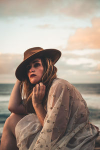 Young woman looking away while sitting on sea against sky