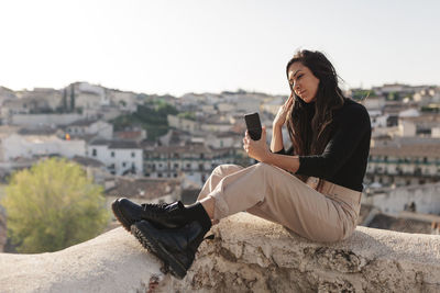 Young woman using mobile phone against sky