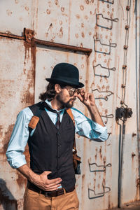 Young man looking away while standing against wall