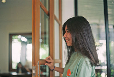 Smiling young woman standing against glass