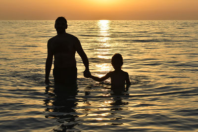 Silhouette friends on sea against sky during sunset