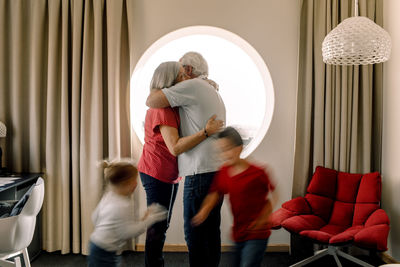 Senior couple embracing while grandchildren playing in room