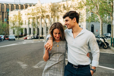 Smiling couple in trendy clothes standing in city street and embracing with love