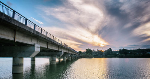 Bridge over river against sky at sunset