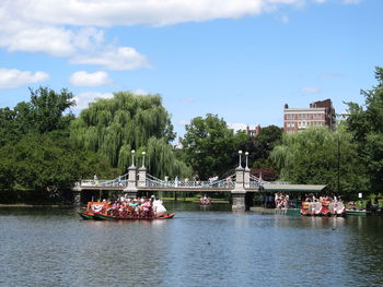 Boats in river by trees against sky