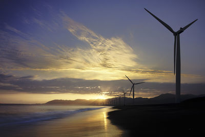 Silhouette wind turbines on landscape against sky during sunset