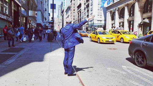 Rear view full length of man hailing on sidewalk in city