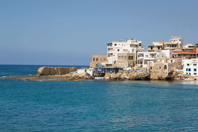 Buildings by sea against clear sky