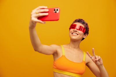 Portrait of young woman using mobile phone against yellow background