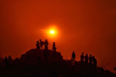 Silhouette people on rock against orange sky