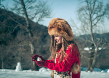 Smiling girl wearing fur hat while holding snow outdoors