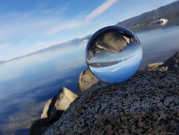 Close-up of crystal ball on rock at beach against sky