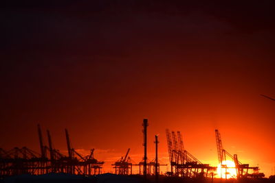 Silhouette cranes at construction site against sky during sunset