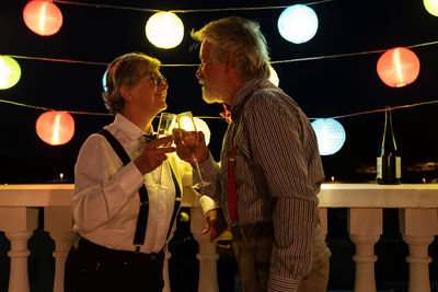 Senior couple drinking wine against illuminated decoration at night