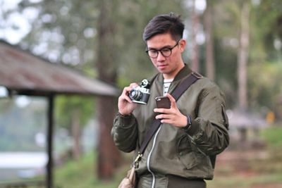 Young man photographing with phone and camera while standing on land