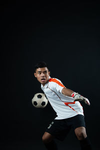 Low angle view of boy playing soccer ball against black background