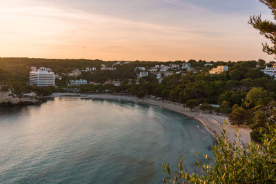 Scenic view of river by buildings against sky at sunset