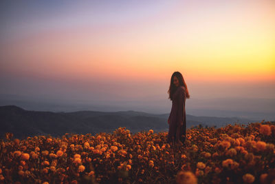 Woman standing on land against sky during sunset