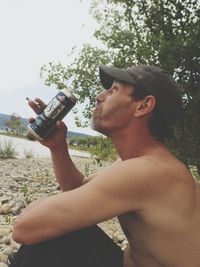 Side view of man drinking water against sky