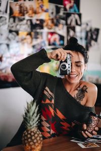 Portrait of smiling woman holding camera while sitting on table