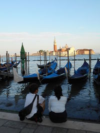 Rear view of men sitting on wooden post in canal