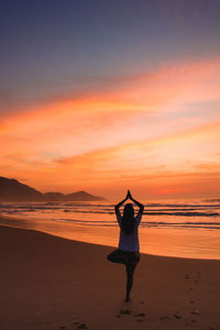 Rear view of man standing at beach during sunset