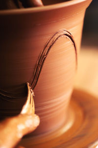 Unrecognizable artisan using fork to scratch wave on clay pot during work in workshop