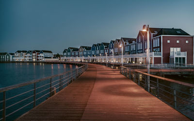 Illuminated pier amidst buildings against sky at dusk