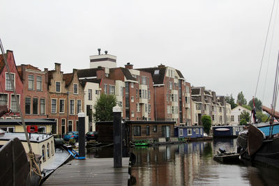 Boats moored in canal by buildings against sky in city