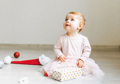 Cute little baby girl in pink dress with tutu skirt and santa hat with present gift box on floor 