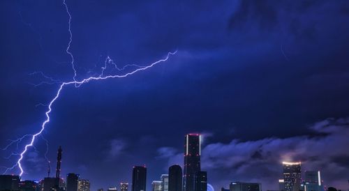 Lightning in sky over city buildings at night