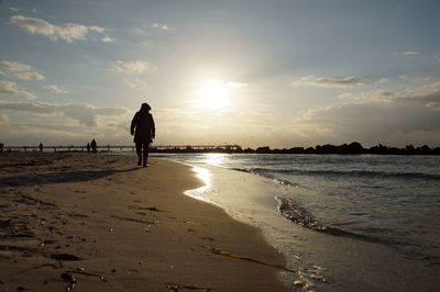 Rear view of silhouette man on beach against sky during sunset