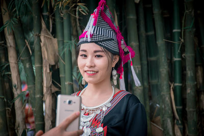 Portrait of smiling woman holding smart phone while standing outdoors