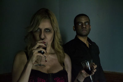 Portrait of people holding wineglasses standing against wall at home