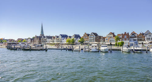 Sailboats in canal by buildings against clear sky