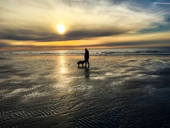 Silhouette people on beach against sky during sunset