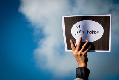 Cropped hand of person holding text on paper against sky