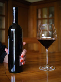 Close-up of woman holding wine bottle by glass on table