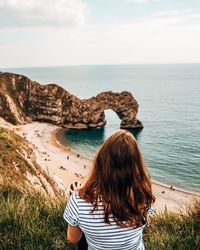 Rear view of woman standing on rock by sea against sky