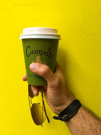 Close-up of hand holding drink against yellow wall