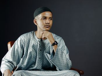 Young man sitting against black background