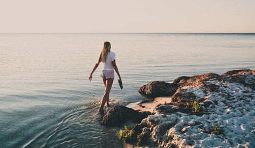 Woman standing on rock at beach against sky