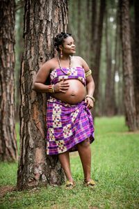 Full length of woman standing by tree trunk in forest