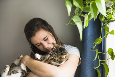 Woman indoors at home cuddling with her cat by the window