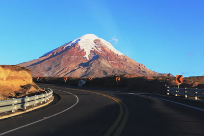 Empty road by mountain against clear sky