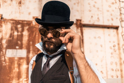 Portrait of man holding hat against wall